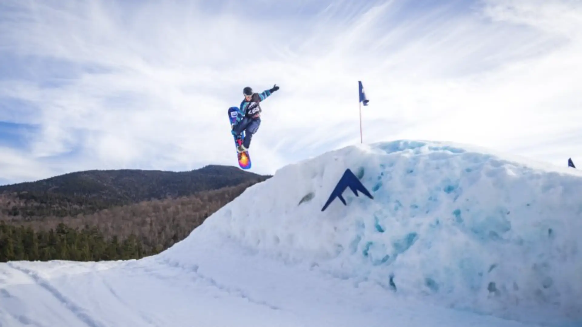 Person on a snowboard does a trick off of a large snow jump with the whiteface logo superimposed in the center